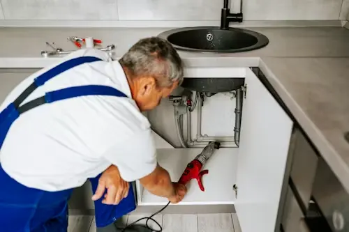 An emergency plumber in Watford repairing a leaking kitchen sink and pipework under a counter.