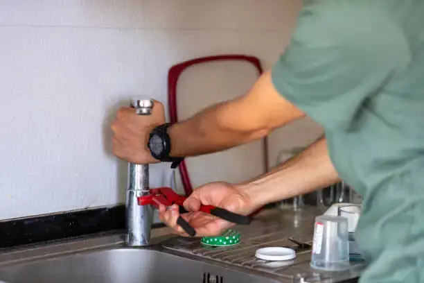 A plumber in Watford using a pipe wrench to repair a kitchen tap and stainless steel sink.