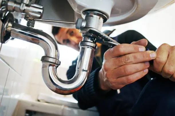 skilled Watford plumber using a wrench to tighten chrome bathroom sink fittings and P-trap.