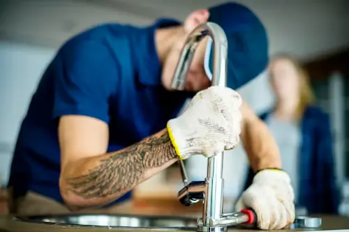 Residential and commercial plumbers in Watford installing a modern chrome mixer tap on a kitchen island.