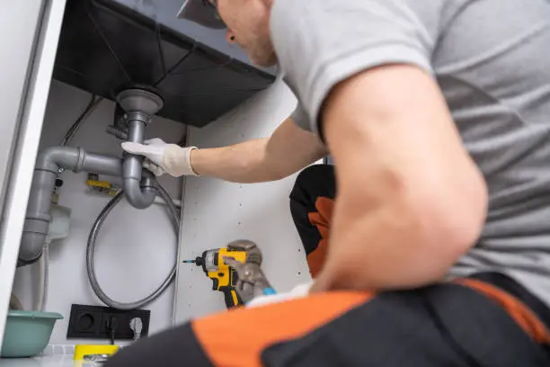 Professional plumbers in Watford installing new drainage pipes and P-trap under a kitchen sink.